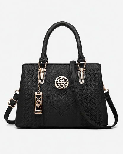 front view of black PORT&LOTUS woven embossed top handle satchel bag detachable crossbody strap vintage gold metal pendant plain white background