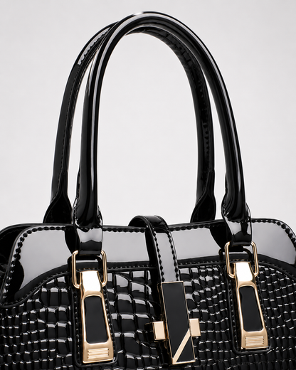Close-up of black PORT&LOTUS patent crocodile embossed handbag with glossy top handles decorative front straps and gold-tone clasp