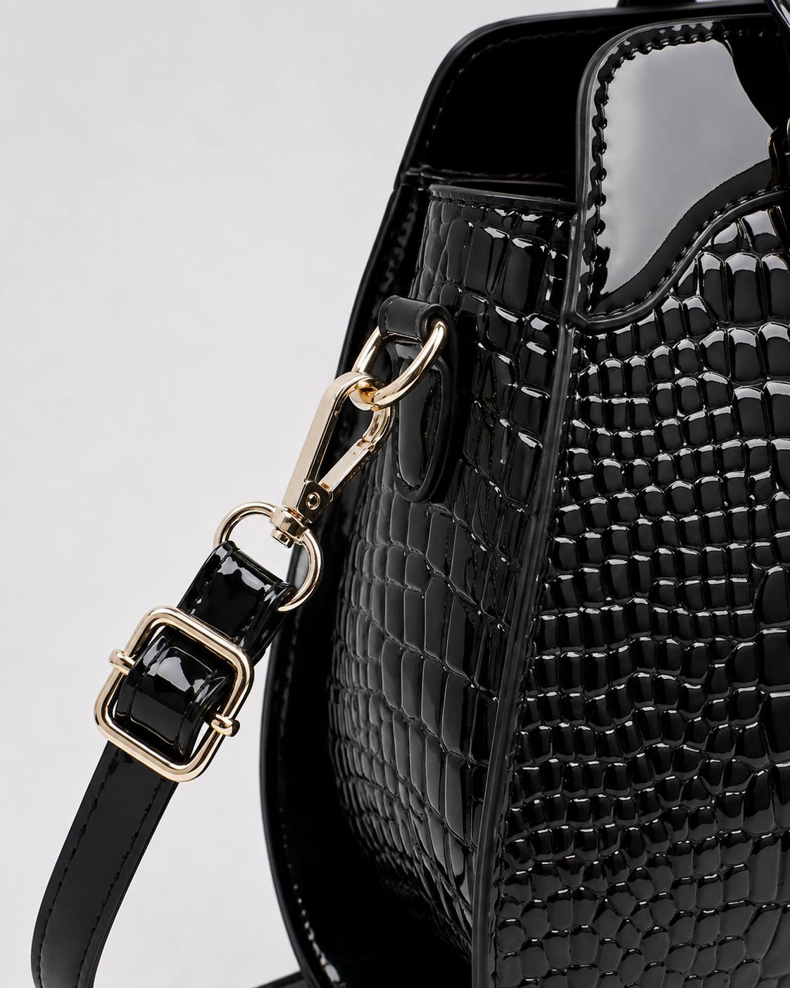 Close-up of black PORT&LOTUS patent crocodile embossed handbag with detachable shoulder strap gold-tone clasp and adjustable buckle