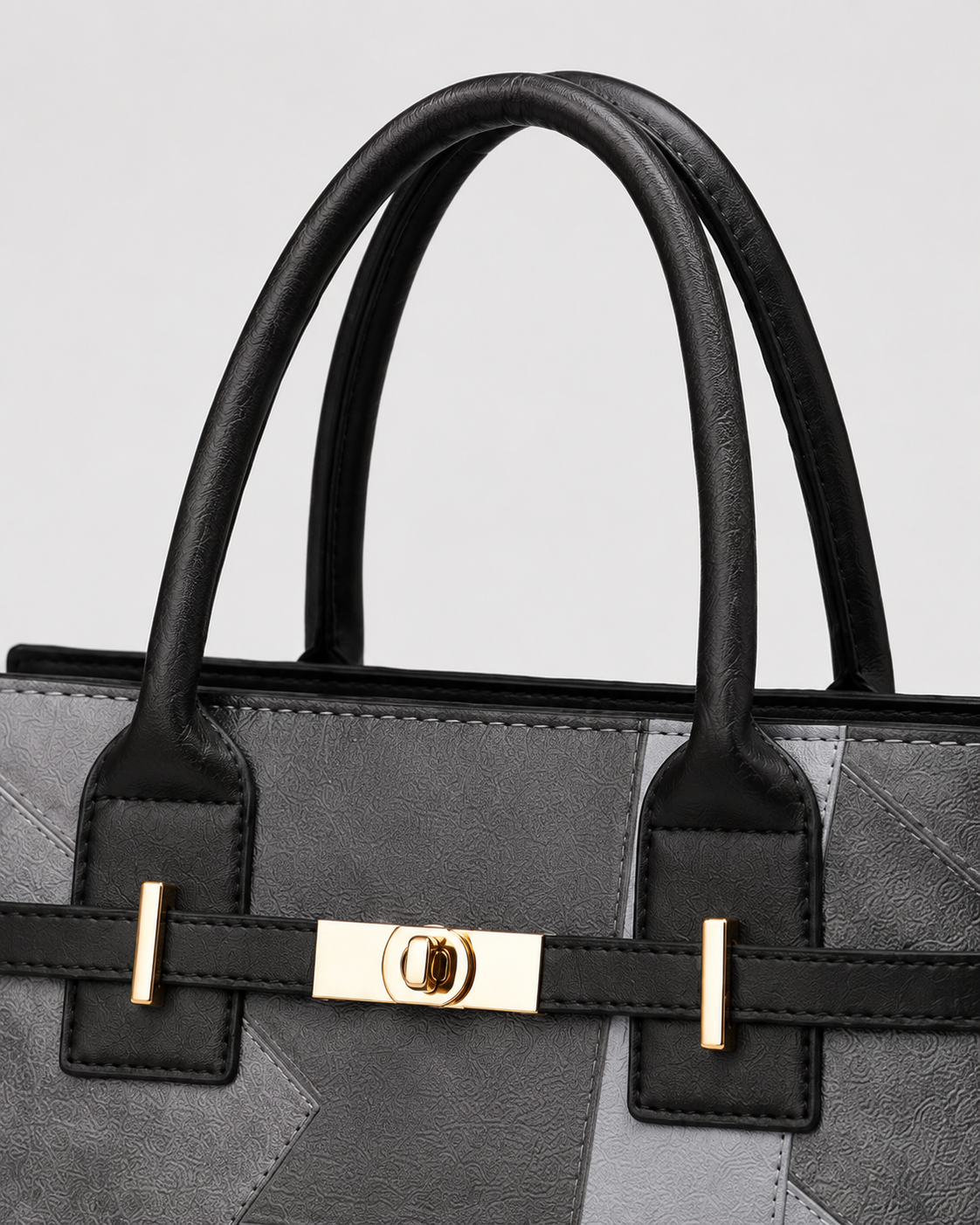 Close-up of gray patchwork tote handbag with black padded handles and polished gold-tone front turn-lock closure
