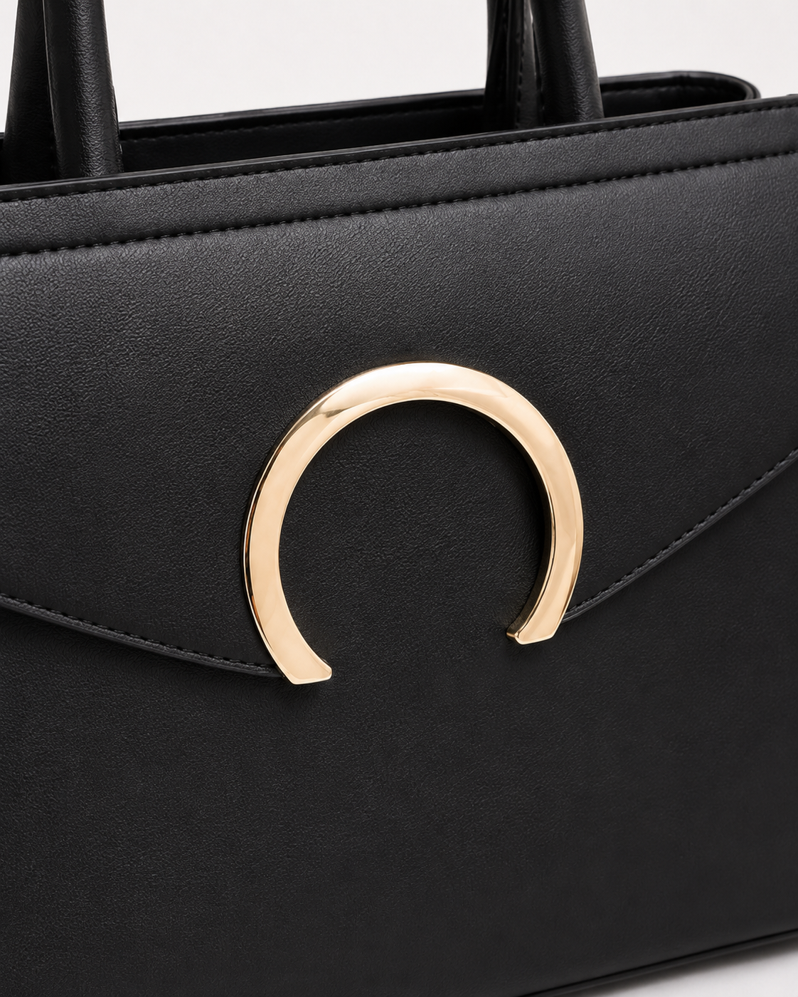 Close-up of black PORT&LOTUS tote bag with polished gold-tone crescent closure smooth vegan leather and flap stitching