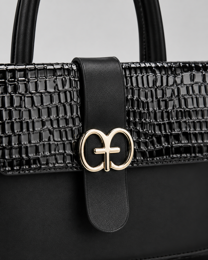 Close-up of black PORT&LOTUS handbag with black and pink crocodile embossed flap smooth vegan leather center strap and gold-tone clasp
