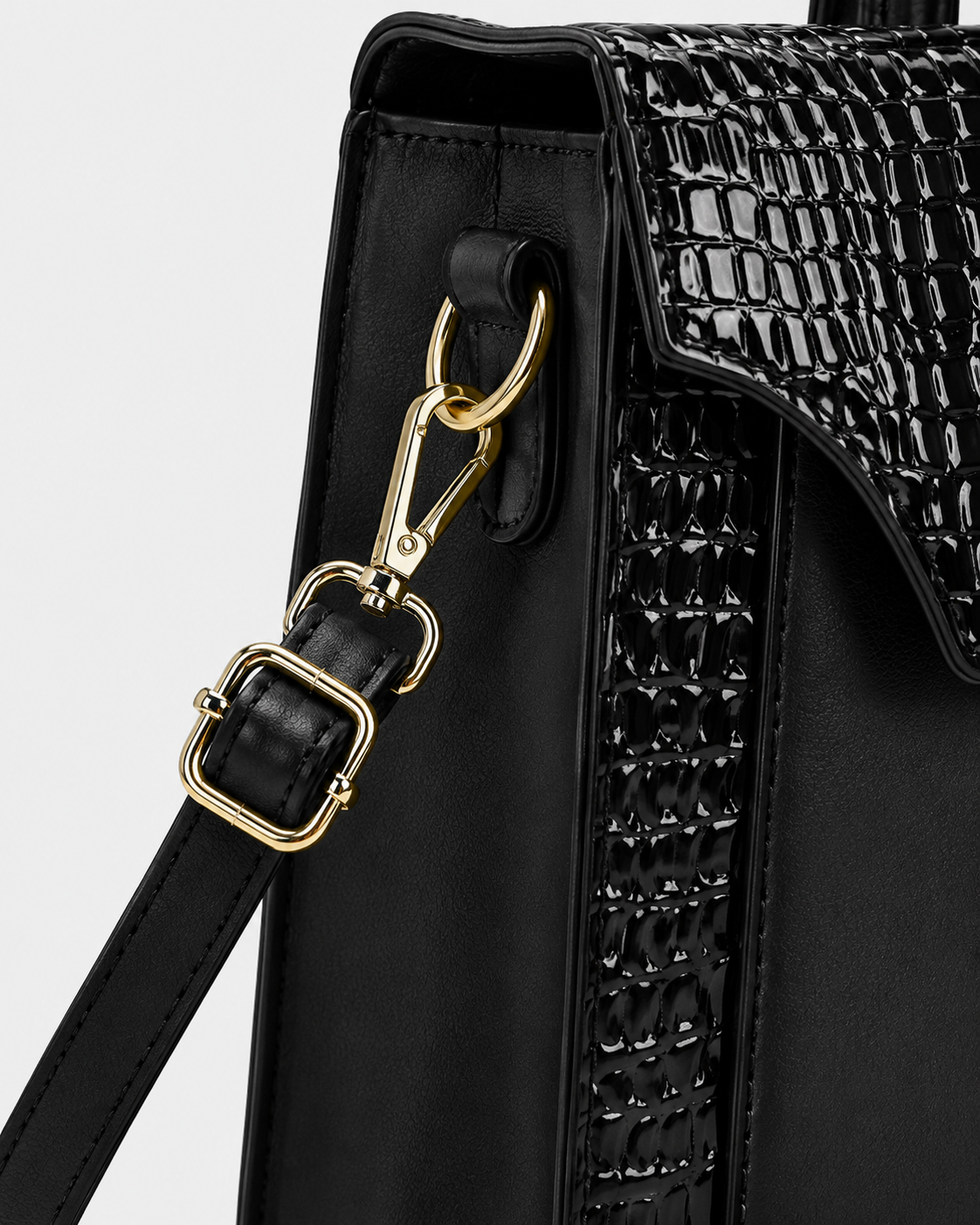 Close-up of black PORT&LOTUS handbag side panel with crocodile embossed trim detachable shoulder strap gold-tone clasp and adjustable buckle