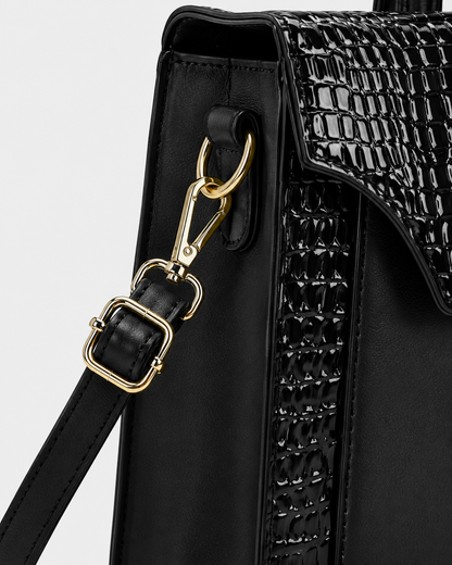 Close-up of black PORT&LOTUS handbag side panel with crocodile embossed trim detachable shoulder strap gold-tone clasp and adjustable buckle
