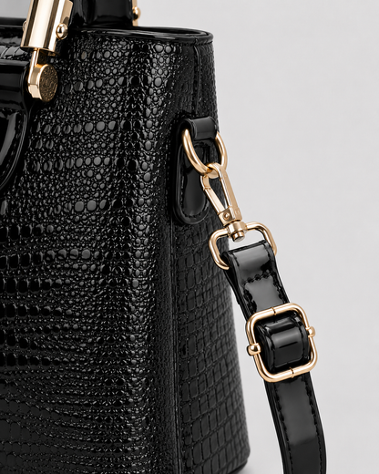 Close-up of black crocodile embossed handbag with detachable shoulder strap adjustable buckle and gold-tone clasp