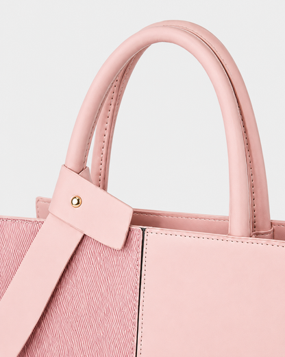 Close-up of pink tote bag with padded double handles, decorative bow accent, gold-tone stud and precise stitching
