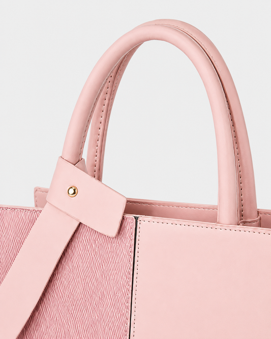 Close-up of pink tote bag with padded double handles, decorative bow accent, gold-tone stud and precise stitching